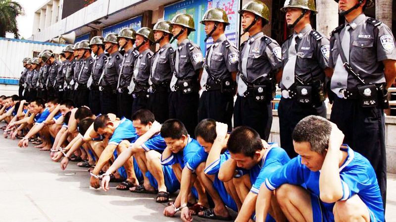 Chinese policemen stand over a group of men convicted of crimes during public sentencing in front of a train station in China's southern city of Guangzhou, June 20, 2002. The convicted were sentenced to labour camps for "re-education". ?? OUT - RTXLBRI