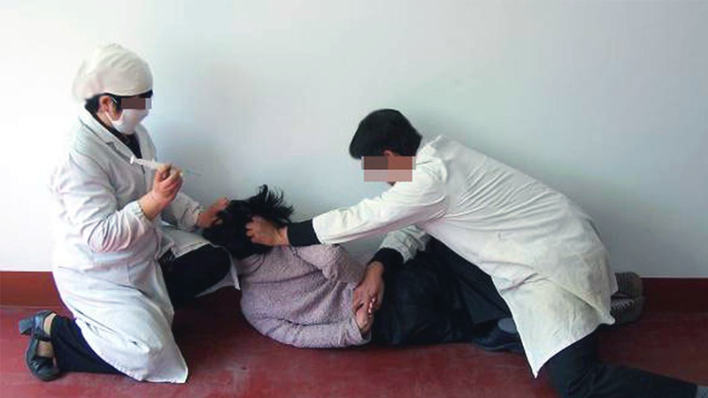Tái hiện cảnh một nạn nhân bị ép tiêm thuốc không rõ nguồn gốc. (Ảnh: Minghui.org)